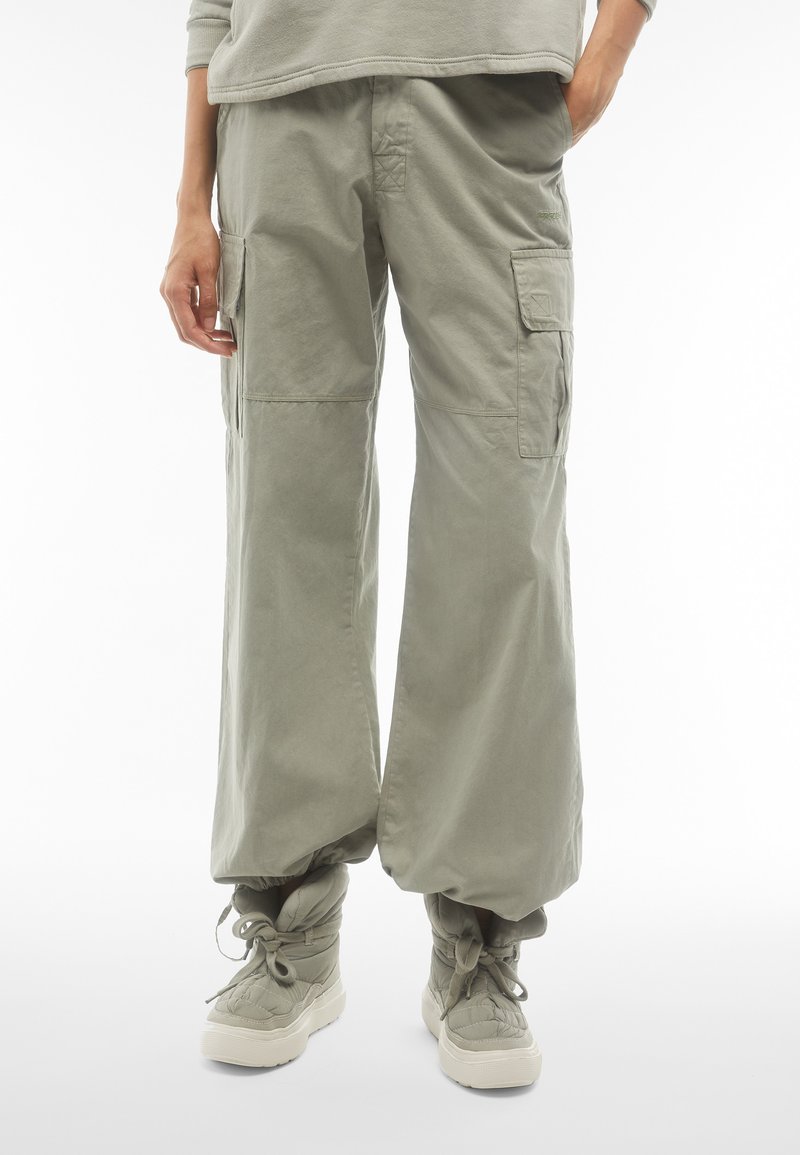 Pantaloni cargo morbidi in cotone verde chiaro, con molteplici tasche laterali, polsini elasticizzati e una consistenza morbida abbinati a stivaletti imbottiti.