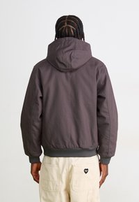 Hooded jacket in dark gray fabric, featuring a relaxed fit. Ribbed cuffs and hem, with smooth texture and minimalistic design.