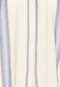 Chemise blanche à rayures verticales bleues et argentées, avec un devant à boutons et un tissu texturé, présentant un motif cousu.