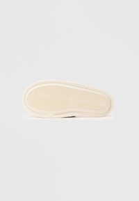 Talpă din cauciuc de culoare crem cu striuri texturate și logo. Formă rotundă, design plat și o mică gaură aproape de margine.
