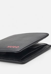 Portofel din piele neagră cu un finisaj texturat, având un logo roz "HUGO". Deschis, dezvăluie sloturi pentru carduri și un design elegant.
