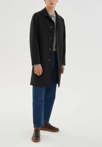 Mustast mantlist esiküljel nööpidega, pikad varrukad ja sirge lõige. Kantud üle halli särgi, kombineeritud siniste teksade ja pruuni tossudega.