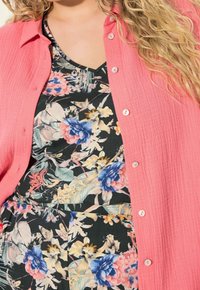 Pink, textured button-up shirt layered over a black floral print dress featuring blue and pink flowers. Buttons are round and white.
