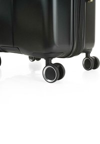 Maleta rígida negra con acabado texturizado, que cuenta con un cierre de doble cremallera y cuatro ruedas multidireccionales con acentos plateados.