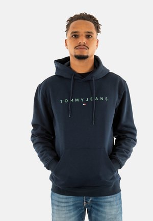 Navyblauwe hoodie van zacht materiaal, met een voorzak en een capuchon met trekkoord. "TOMMY JEANS" logo in lichtgroen over de borst.