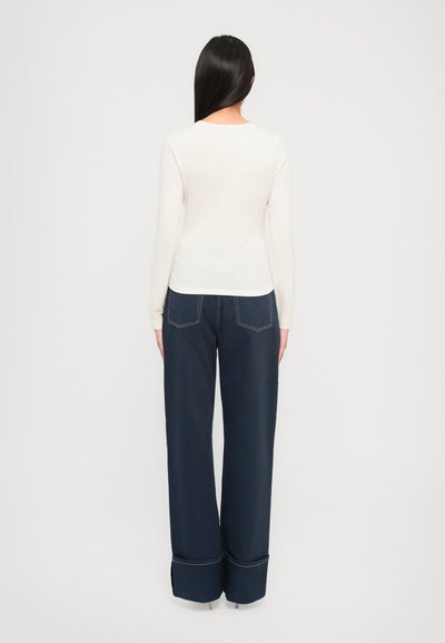 Heledbeez värvi pika varrukaga pluus, mille vöökoht on kitsas, koos laia tumedama sinise lõdva püksega, millel on nähtavad õmblused ja laiad allääred.