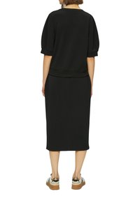 Ensemble de sweat-shirt noir et jupe assortie, offrant des manches bouffantes courtes et une coupe décontractée. Le tissu est lisse, avec un ourlet au genou.
