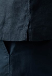 Tela oscura con un patrón de espiga texturizado. Presenta costuras visibles y una abertura lateral. El material parece ligero y suave.