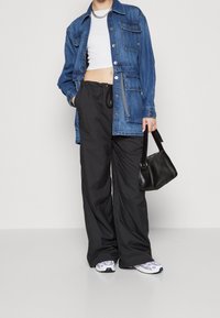 Veste en denim, cropped top blanc, pantalon large noir et baskets avec accents violets ; portant un petit sac à main noir.