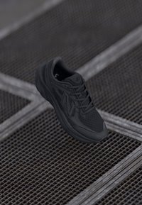 Black running shoe featuring mesh upper, textured sole, and flexible design. Prominent 'N' logo on side, laces, and cushioned heel.