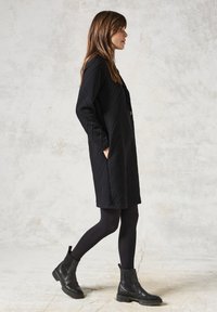 Zwarte gequiltte jas met ruitpatroon, met lange mouwen, zijzakken en een losse pasvorm, gecombineerd met zwarte maillots en enkellaarsjes.