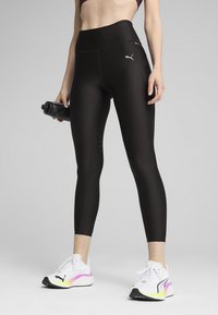 Fekete sportleggings magas derékkal, kényelmes illeszkedéssel és diszkrét fényvisszaverő részletekkel, fehér cipőkkel, amelyek gradiens mintázattal rendelkeznek.