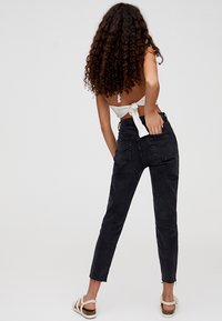 Jean en denim noir à taille haute, jambes fuselées et ourlet effiloché. Comprend quatre poches et des détails de couture subtils.