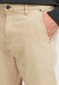 Beige katoenen broek met zijzakken, een knoopsluiting en een gestructureerde stof. Het ontwerp heeft zichtbare stiksels en een klassieke pasvorm.