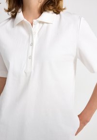 Hvid bomulds polo shirt med blød krave, tre knaplukninger og korte ærmer. Glat tekstur med en afslappet pasform og uden mønstre.