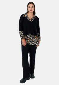 Un pull court en tricot noir superposé sur une chemise à imprimé léopard, associé à un pantalon noir et des chaussures noires imposantes. Design simple et texturé.