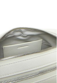 Interno di una borsa in pelle bianca testurizzata con chiusura a cerniera in argento. Include uno scomparto per schede e una fodera morbida. Dettagli di design minimalisti.