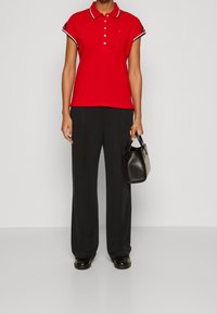 Röd polo T-shirt med vita och svarta accenter, korta ärmar och tre knappar, kombinerad med svarta vida byxor och en liten svart handväska.