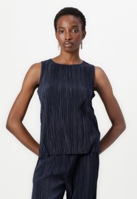 Haut sans manches bleu marine avec des plis verticaux, encolure ronde et coupe décontractée. Le tissu a une texture lisse. Associé à un pantalon assorti.