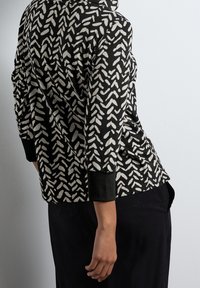 Černobíle vzorovaná bunda s hladkou texturou, se vzorem listů, dlouhými rukávy a mírně volným střihem.
