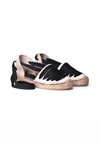 Mustat ja valkoiset espadrillot, joissa on kudottu kangas yläosa, leikattuja yksityiskohtia ja juuttikuvioiset pohjat. Pitkät mustat nauhat turvallista istuvuutta varten.