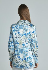 Blusa floral con un patrón en azul, verde y blanco, hecha de una tela suave con mangas largas y un cuello clásico.