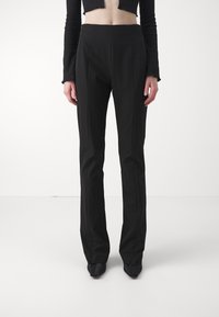 Pantalons noirs ajustés à taille haute, jambes droites et plis avant subtils, fabriqués en tissu lisse. Assortis à un haut noir ajusté.