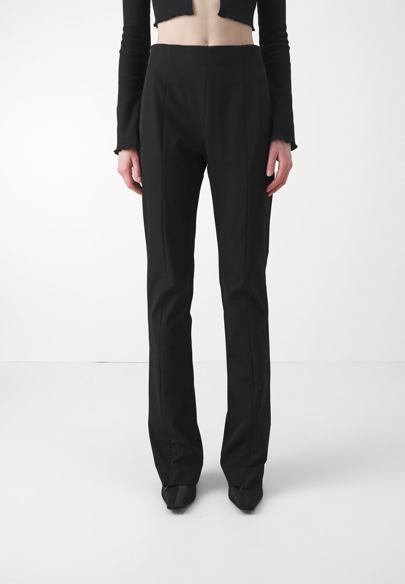 Pantalons noirs ajustés à taille haute, jambes droites et plis avant subtils, fabriqués en tissu lisse. Assortis à un haut noir ajusté.