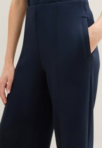 Pantalones de pierna ancha azul marino, elaborados con tela suave, que cuentan con un frente plano, bolsillos laterales y detalles cosidos en la parte delantera.