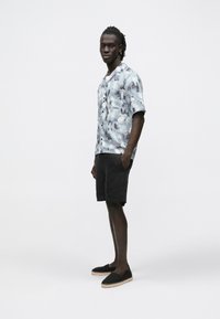 Camisa de manga curta, azul com padrão cinza, combinada com calções e alpargatas pretas. Apresenta um corte descontraído e fecho de botões na camisa.