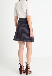 Knit cream sweater yang pas dipadukan dengan rok navy sepanjang lutut yang memiliki garis diagonal merah dan putih. Sandal hak tinggi berwarna cokelat melengkapi penampilan ini.