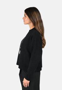 Sweater noir raccourci à coupe loose, avec des poignets et un col côtelés. Assorti avec un pantalon noir taille haute, montrant un profil latéral.