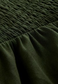 Zielona tkanina o fakturze z marszczeniem. Materiał wydaje się miękki z lekko błyszczącym wykończeniem, podkreślającym fałdy i zmarszczki.