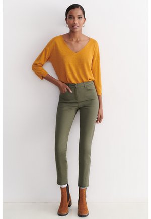 Sennepsfarvet V-hals striktop med trekvartærmer, parret med højhalsede olivengrønne bukser og brune ankelstøvler. Glatte teksturer.