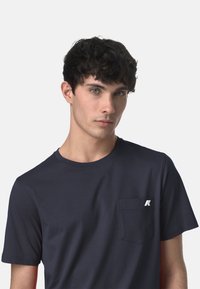 T-shirt a maniche corte blu navy realizzato in cotone morbido, dotato di una tasca sul petto con un logo bianco. Tessuto morbido e design classico con colletto a girocollo.