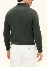 Mörkgrön tröja med krage, långa ärmar och ribbade muddar. Bärs med vita byxor som visar en slät stickad textur.