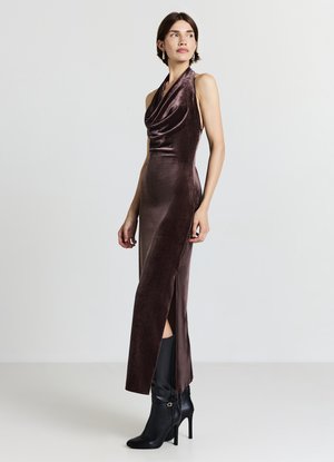 Abito in velluto con collo all'americana di colore marrone scuro, con davanti drappeggiato, spacco laterale e vestibilità aderente, abbinato a stivali neri con tacco alto.