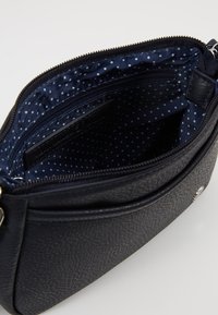 Borsa in pelle nera con finitura texture e chiusura a zip, dotata di un interno a pois blu, tasca laterale e dettagli in hardware argentato.
