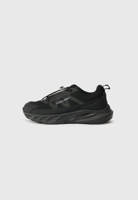 Chaussure de sport noire avec une tige en mesh texturé, semelle en caoutchouc épaisse, système de laçage ajustable et logo sur le côté.