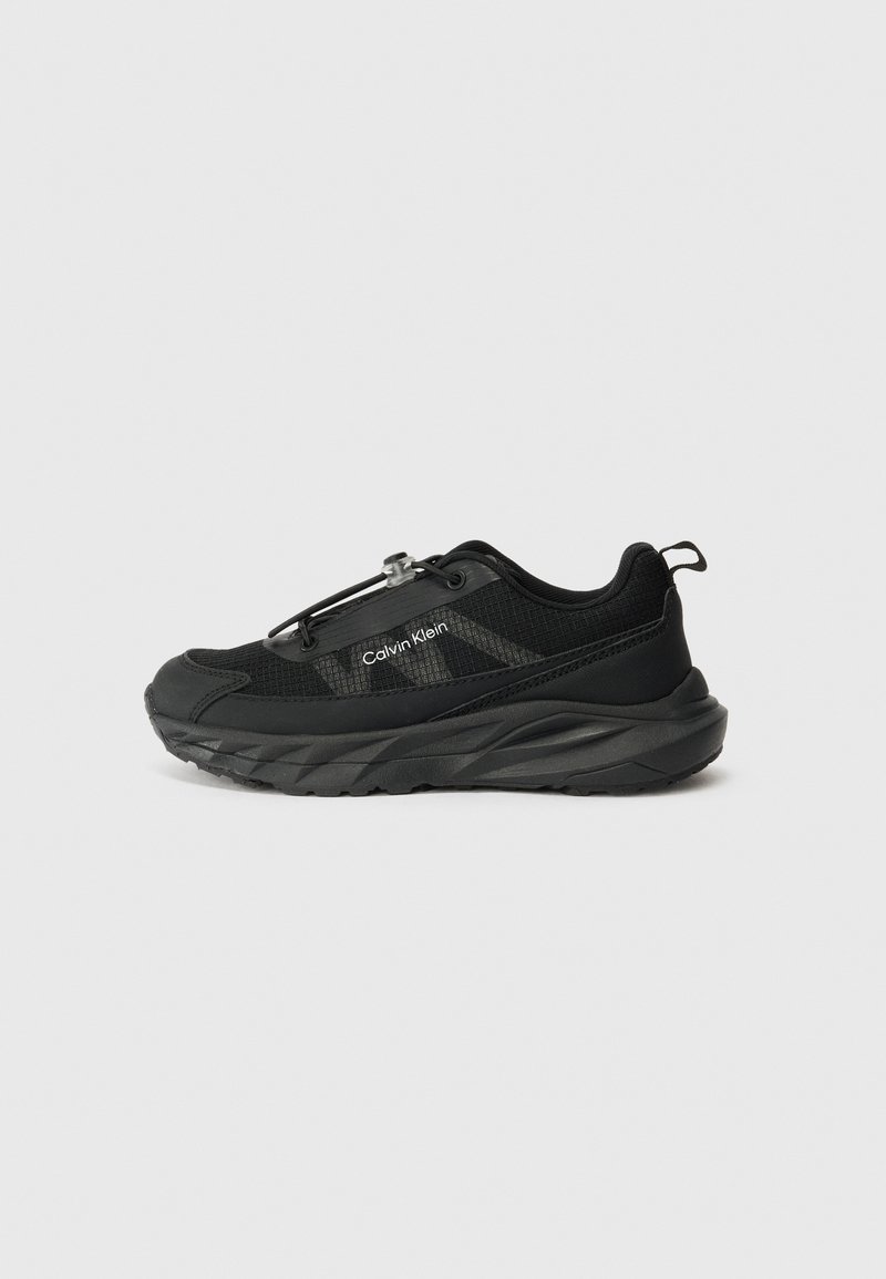 Chaussure de sport noire avec une tige en mesh texturé, semelle en caoutchouc épaisse, système de laçage ajustable et logo sur le côté.