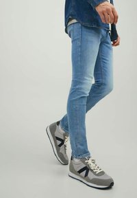 Jeans ajustados de color azul claro con detalles desgastados, combinados con zapatillas grises y blancas con acentos en azul marino y superposiciones texturizadas.