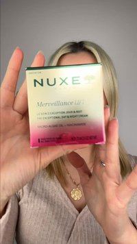 Blond persoon houdt een doos met Nuxe Merveillance Lift dag- en nachtcrème met microalgenolie en niacinamide dicht bij de camera.