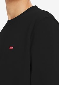 Zwarte katoenen sweatshirt met een ronde hals, met een klein rood Levi's-logo op de linkerborst. Gladde textuur en aangesloten mouwen.