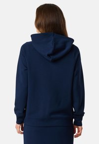 Navy blauwe hoodie van zacht materiaal, met een grote capuchon, ribgebreide manchetten en onderrand. Achteraanzicht toont een gladde textuur en een relaxte pasvorm.