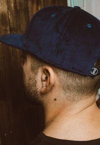 Cappello in corda blu navy con visiera piatta, caratterizzato da una piccola toppa con logo sul lato e cuciture blu a contrasto su una superficie texturizzata.
