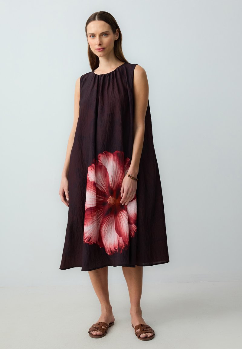Mouwloze zwarte jurk met een grote roze en witte bloemenprint aan de voorkant, gemaakt van lichtgewicht stof, met een losse A-lijn silhoutte.