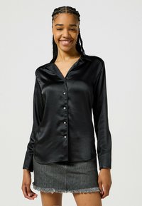 Czarna satynowa koszula z guzikiem i kołnierzykiem, z perłowymi guzikami i długimi rękawami. Noszona z szaro-denimową mini spódniczką z postrzępionymi brzegami.