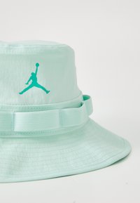 Sombrero de cubo verde menta con ala ancha, con un acabado texturizado y un prominente logo turquesa de Jordan en la banda frontal.
