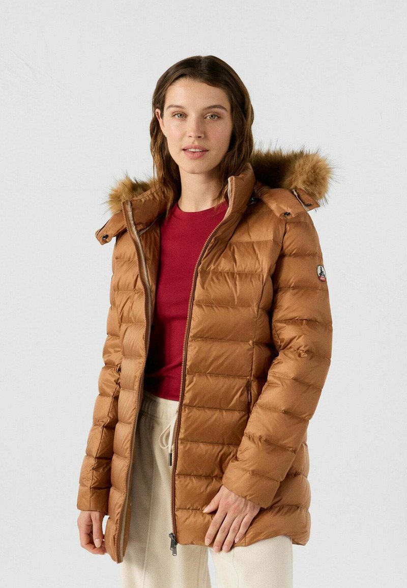 Giacca a piumino marrone con cuciture orizzontali, cappuccio con bordo in pelliccia, chiusura frontale con cerniera e tasche laterali. Indossata sopra una maglia rossa.