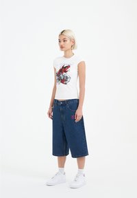 White short-sleeve t-shirt with a red fish graphic; paired with blue denim culottes and white sneakers. Simple, relaxed fit design.